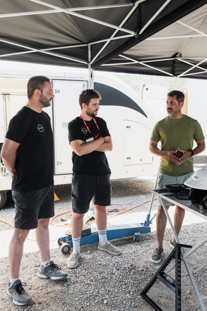Drei Nissan Teammitglieder stehen in einem Nissan Pavillon auf einem Schotterboden