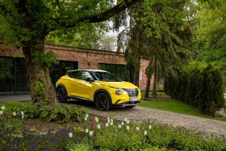 Żółty Nissan Juke stojący bokiem na tle budynku i drzew
