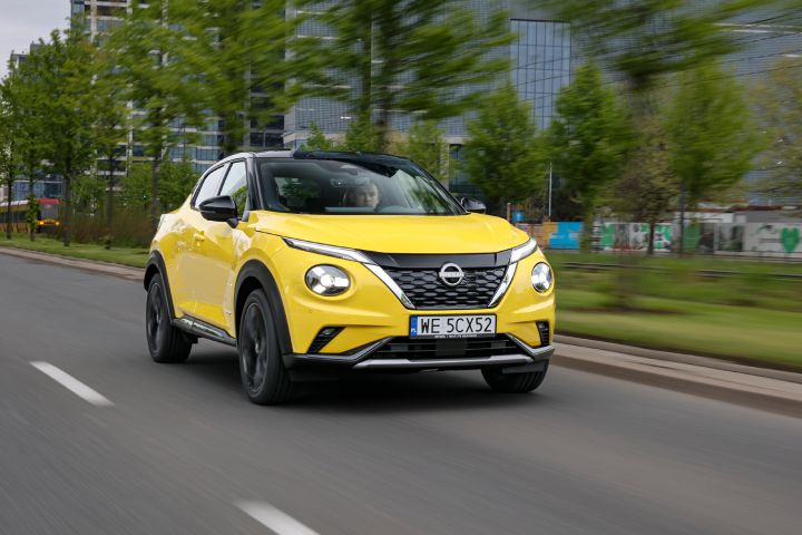 Jadący żółty Nissan Juke (widok z półprofilu) z budynkami w tle