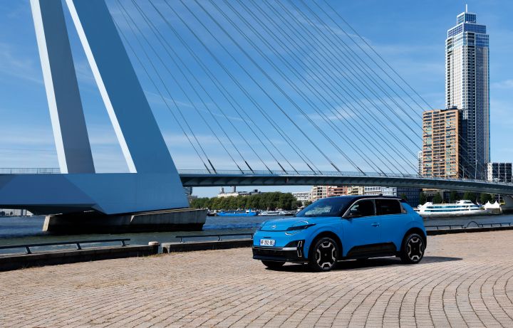 Seitenansicht eines Nissan Micra auf einem hell gepflasterten Platz im Sonnenschein vor einer Brücke und einem Hochhaus in Rotterdam