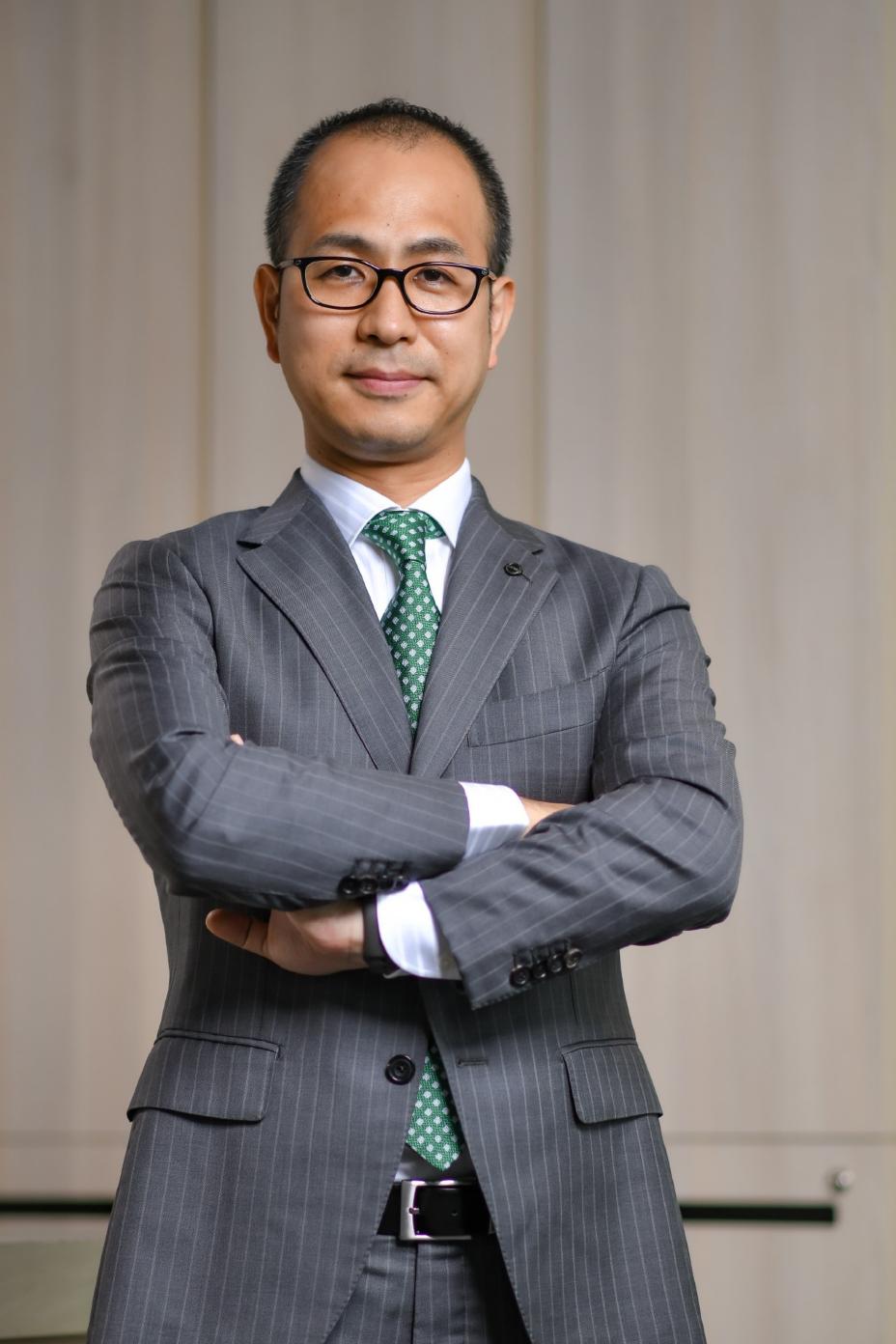A photo of Masao Tsutsumi wearing a suit with his arms crossed