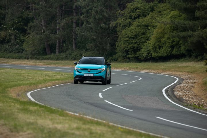 Une nouvelle Nissan LEAF bleu turquoise roule sur une route sinueuse avec un fond de verdure