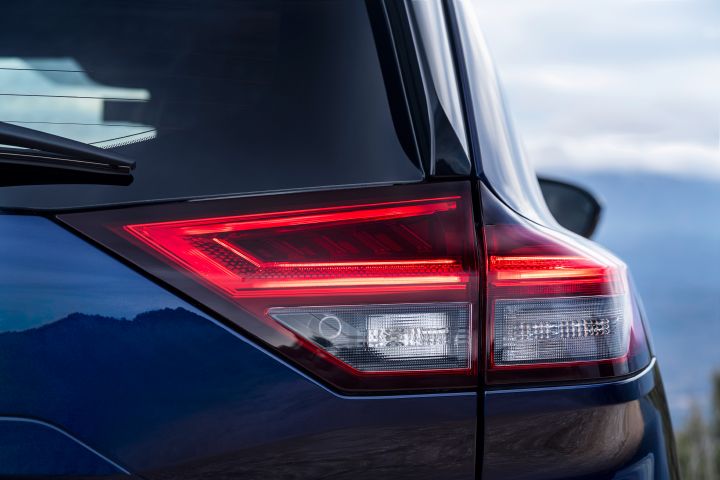 Nahaufnahme der Rückleuchten des neuen 2026 Nissan X‑Trail, die ein modernes, eckiges LED-Lichtdesign mit roten und weißen Bereichen zeigen. Der Hintergrund zeigt eine verschwommene Berglandschaft unter einem bewölkten Himmel, wodurch die Fahrzeugdetails und die Außenumgebung betont werden.