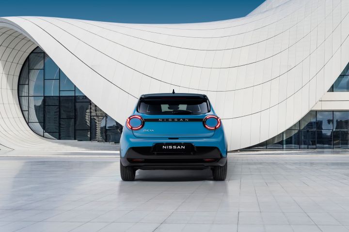 Rear view of gear blue body color & black roof Micra parked in front of a blue & white design architectural building