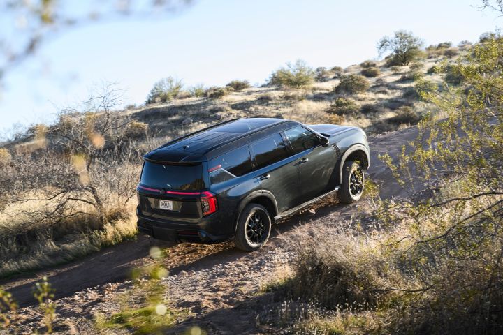 Aerial, side angle view of a 2025 Nissan Armada PRO-4X driving along arid terrain on the side of a hill.