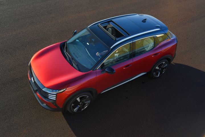 Novo Nissan Kicks Platinum vermelho com teto preto estacionado em frente a uma construção de tijolos aparentes. A foto destaca a traseira e a lateral do SUV, com lanternas em LED, rodas de liga leve e detalhes em preto na carroceria.