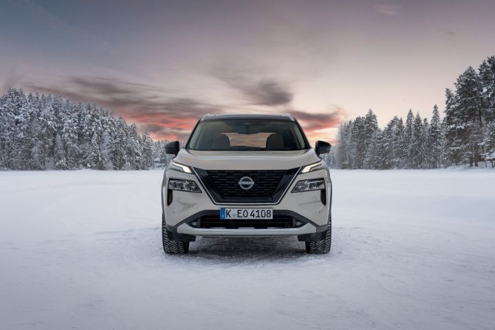 Silberner Nissan X‑Trail e‑Power e‑4ORCE steht auf schneebedecktem Eissee mit verschneiten Bäumen im Hintergrund, Front