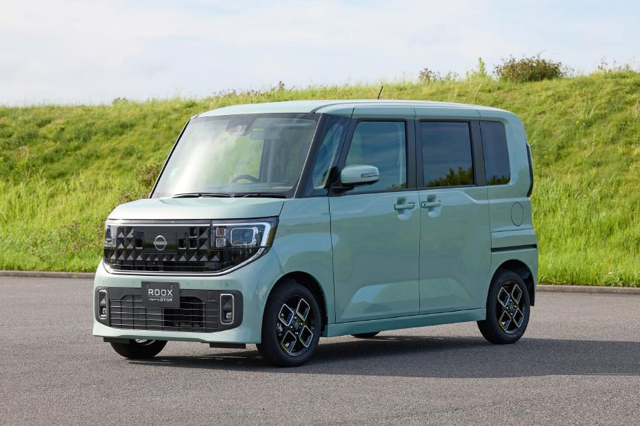 The new Nissan Roox kei car in celadon green is parked against a backdrop of green grass. Its boxy shape stands out while blending harmoniously with the natural surroundings, creating a calm and balanced impression.