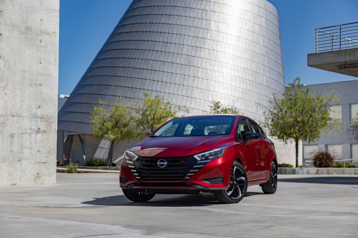 2024 red Nissan Versa parked on a slant in front of a modern stone structure.
