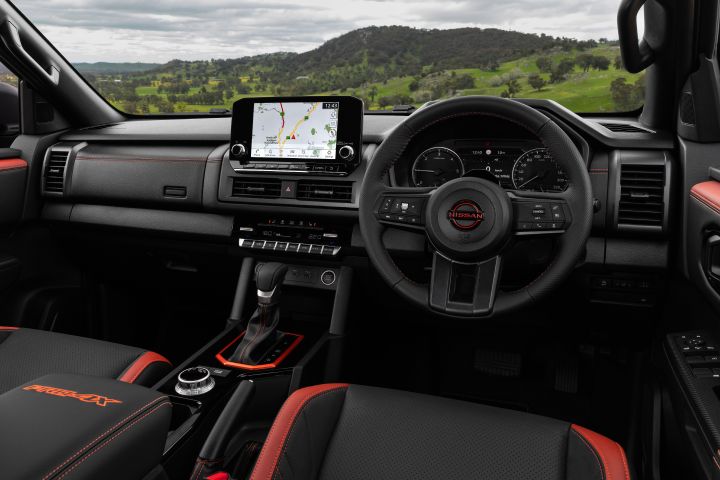 2026 Nissan Navara PRO-4X finished in Boulder Grey featuring a wide cabin view with dashboard, infotainment screen, steering wheel and red-accented front seats.