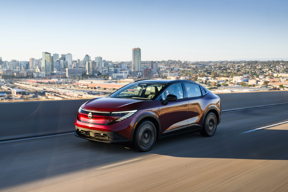 Front left 3/4 view of the 2026 Nissan LEAF driving along a city highway.