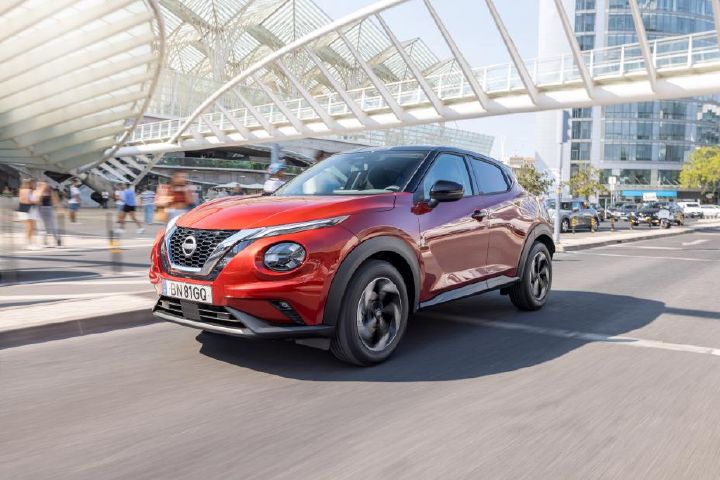 Nissan Juke vermelho, visto de frente, de lado, em rua com edifício por trás