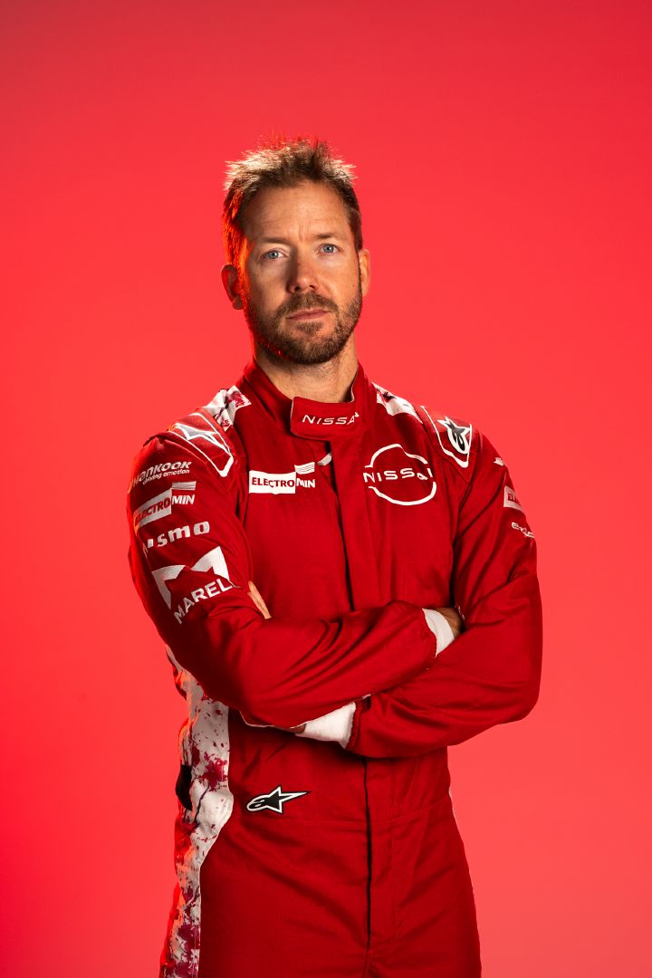 Sam Bird mit verschränkten Armen in seinem roten Rennanzug des Nissan Formula E Teams vor einem roten Hintergrund.
