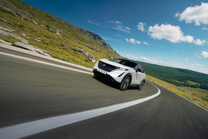 White Ariya driving in front of green mountains