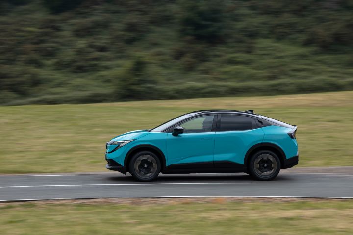 Vue de profil d'une Nissan LEAF en mouvement avec une carrosserie bleu turquoise et un toit en verre flottant noir sur une route sur fond vert