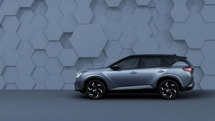 Against a geometric-patterned wall, a silver X‑Trail / Rogue is shown from the side, facing to the right in a calm, studio-like setting.