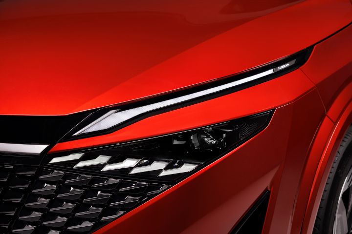 Gros plan sur feu avant-gauche et un bout de la calandre d’un Qashqai rouge Fuji