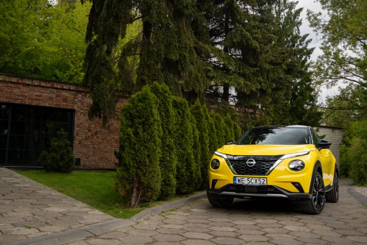Żółty Nissan Juke stojący przodem na tle budynku i drzew