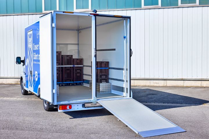 Blick von schräg hinten auf den Nissan Interstar-e mit Bäckereikoffer, beide Heckhälften sind geöffnet, die rechte Hälfte ist als Laderampe schräg zum Boden herabgelassen