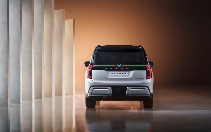 A white Patrol SUV is photographed from the rear, highlighting its refined design and modern taillights. The background features a minimalist space with vertically aligned light pillars.