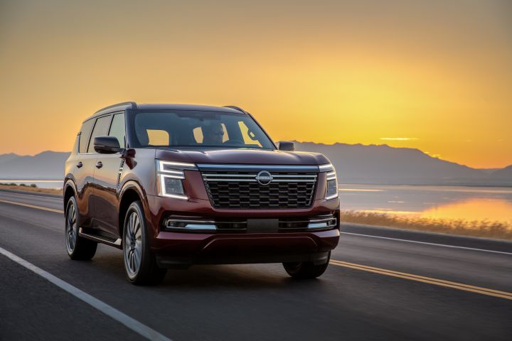 Front right 3/4 angle of a red 2025 Nissan Armada driving on a road with during sunset with a mountain and body of water behind.