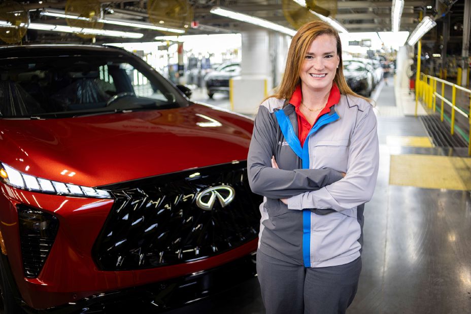 JS Bolton wearing a Nissan manufacturing shirt, standing in front of a Nissan vehicle with her arms crossed.