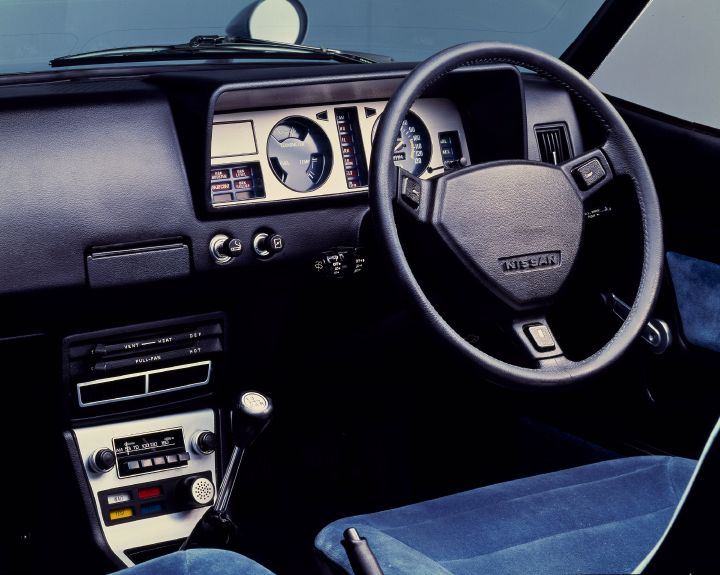 interior view of the drivers seat of a vintage nissan vehicle, with the dashboard, steering wheel and radio shown.