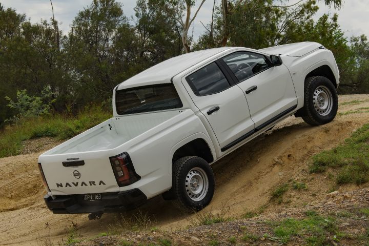2026 Nissan Navara SL dual cab ute finished in Alpine White photographed from the rear-left on a sandy descent, revealing the cargo tub interior and tailgate embossing.