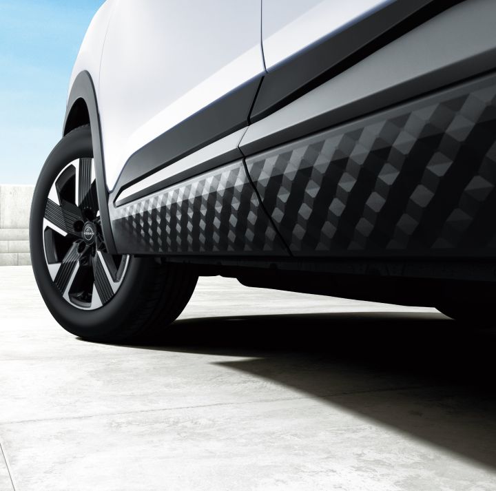 Close-up of the lower side of the Nissan Kicks. The vehicle faces right, emphasizing the sculpted door line and wheel area. The background is a white floor.