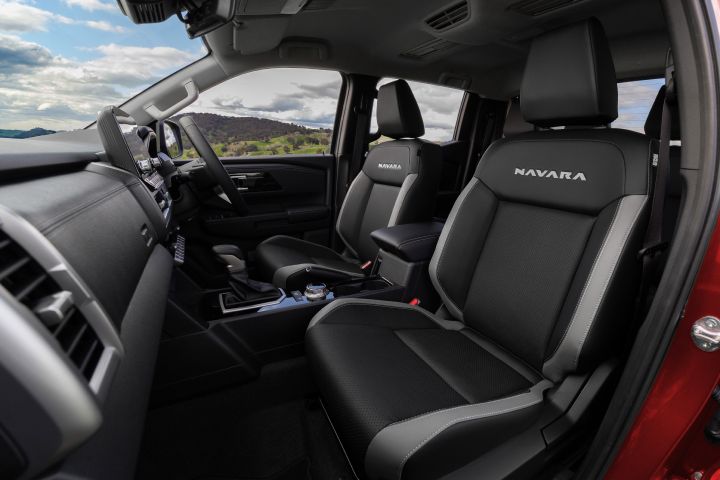 Front seating view inside a 2026 Nissan Navara ST-X, showing the two front seats with NAVARA embroidery, centre armrest, centre console, and dashboard from the passenger side.