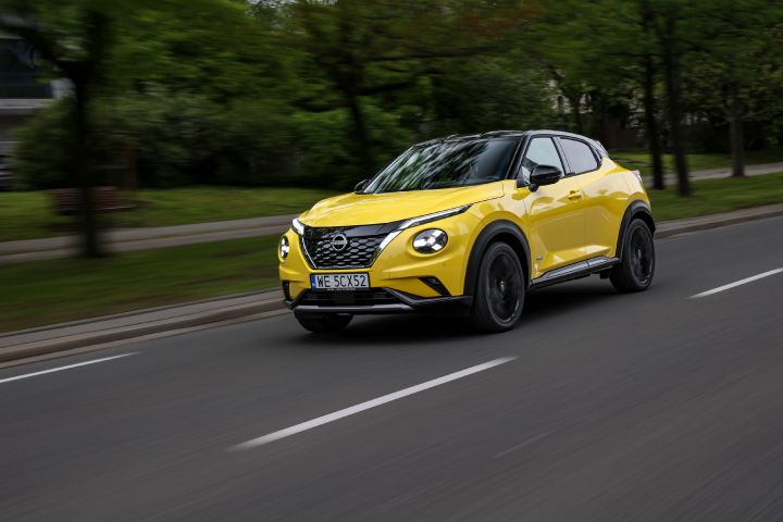 Jadący żółty Nissan Juke (widok z półprofilu) na tle zieleni