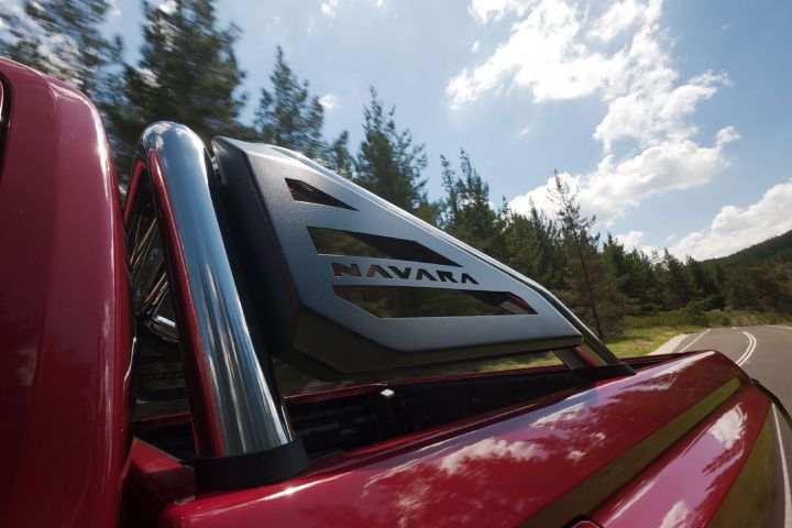 Close-up of the sports bar on a red 2026 Nissan Navara ST‑X, showing chrome uprights and a black panel with the word “NAVARA,” against a background of trees and blue sky.