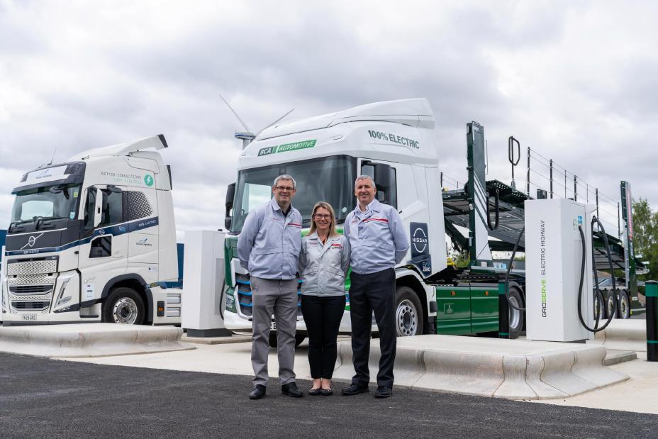 Trois dirigeants de Nissan Sunderland devant deux poids lourds électriques en charge à la nouvelle station de recharge du site