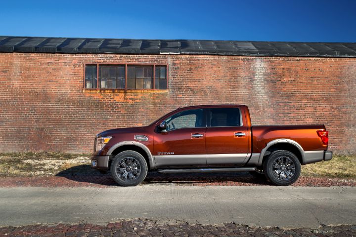 The drivers side profile view of an orange Nissan TITAN parked near a brick building