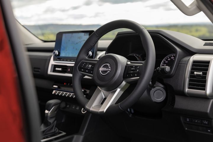 Driver-area view of a 2026 Nissan Navara ST-X interior, showing the steering wheel, instrument binnacle, dashboard, automatic gear selector, and the 9-inch Touch infotainment screen mounted at the centre of the dash.