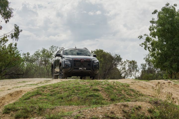 2026 Nissan Navara PRO-4X finished in Boulder Grey head‑on atop a clay crest with prominent grille and lower protection against a cloudy backdrop.