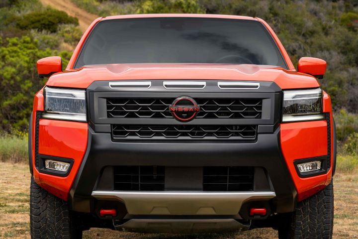 Close up of a red 2025 Nissan Frontier, the grill is black, the Nissan logo and tow hooks remain red.