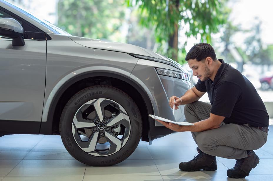 Un técnico de Nissan semi agachado inspecciona a la altura de una rueda una tabla con el programa de revisión.