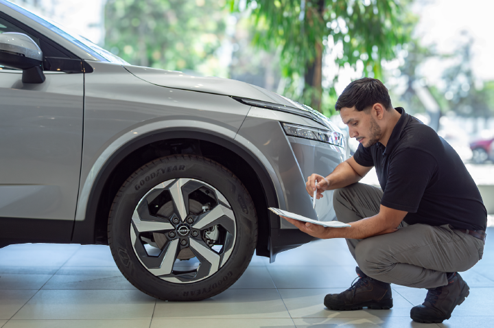 Un técnico de Nissan semi agachado inspecciona a la altura de una rueda una tabla con el programa de revisión.
