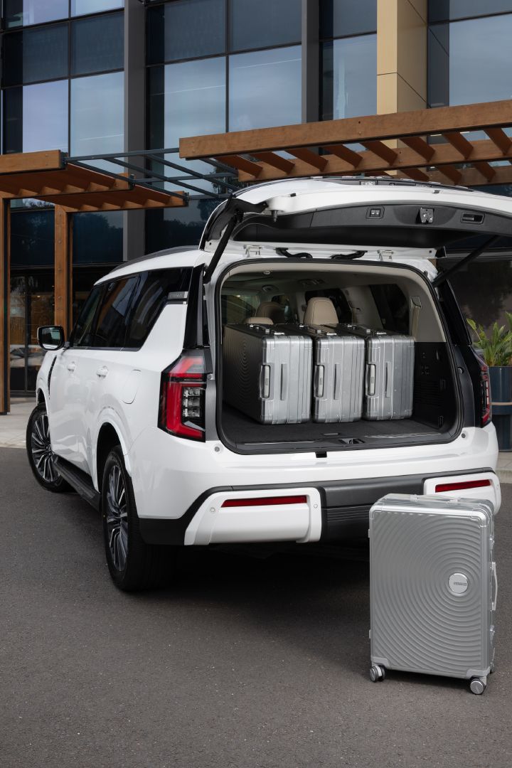 2026 Nissan Y63 Patrol finished in white, shown from a rear three-quarter exterior angle with the tailgate open, four large silver suitcases in the cargo area and another suitcase positioned behind the vehicle.