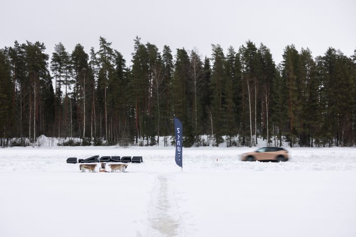 Im Hintergrund fährt das Elektroauto Nissan Ariya e‑4ORCE in Akatsuki Copper mit Dach und Außenspiegel in Pearl Black durch den Schnee Schnee