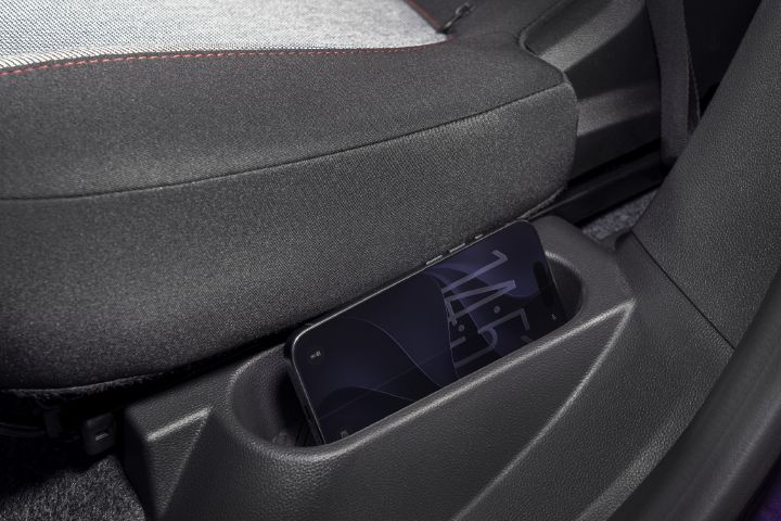 Fotografia que mostra um smartphone colocado num compartimento de arrumação moldado, ao lado de um banco de automóvel. O estofo cinzento escuro e os acabamentos em plástico texturado realçam a conveniência do arrumação do dispositivo no interior do veículo.