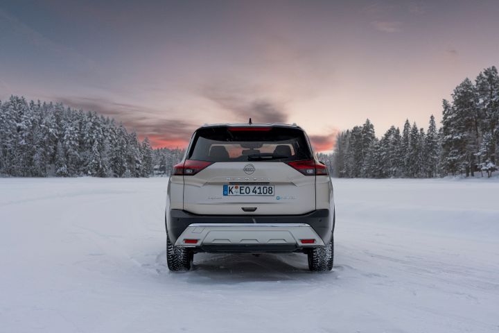 Silberner Nissan X‑Trail e‑Power e‑4ORCE steht auf schneebedecktem Eissee mit verschneiten Bäumen im Hintergrund, Heck