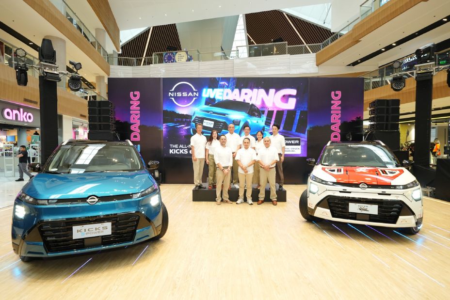 Display of two Nissan vehicles at a shopping mall event, with a group standing on stage in front of a large LED screen.