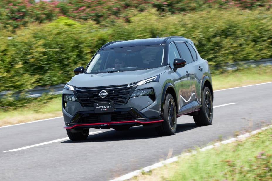 A grey Nissan X-Trail NISMO is driving on a road. The background features greenery and trees.