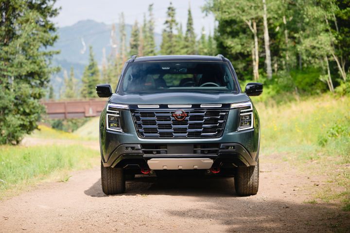 Front view of a 2025 Nissan Armada Pro 4X with the headlights on parked on a dirt path in the woods.