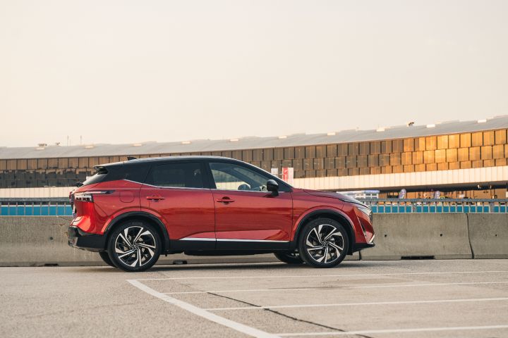 Seitliche Ansicht eines Nissan Qashqai in Fuji Sunset Red auf einem Parkplatz vor Flughafengebäuden