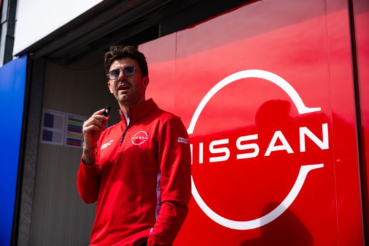 Norman Nato spricht in seinem roten Team-Pullover vor der Teamgarage in ein kleines Mikrofon