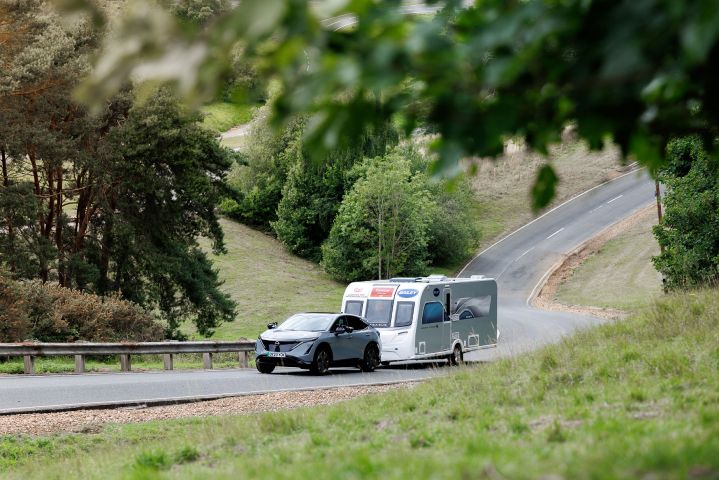 Ariya towing a caravan in the distance through the trees
