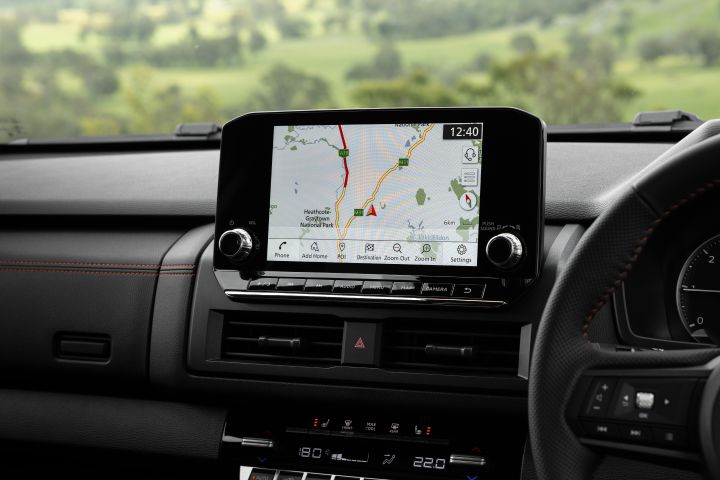 2026 Nissan Navara PRO-4X finished in Boulder Grey featuring the touchscreen navigation display, rotary dials, centre vents, climate controls and a partial steering wheel.